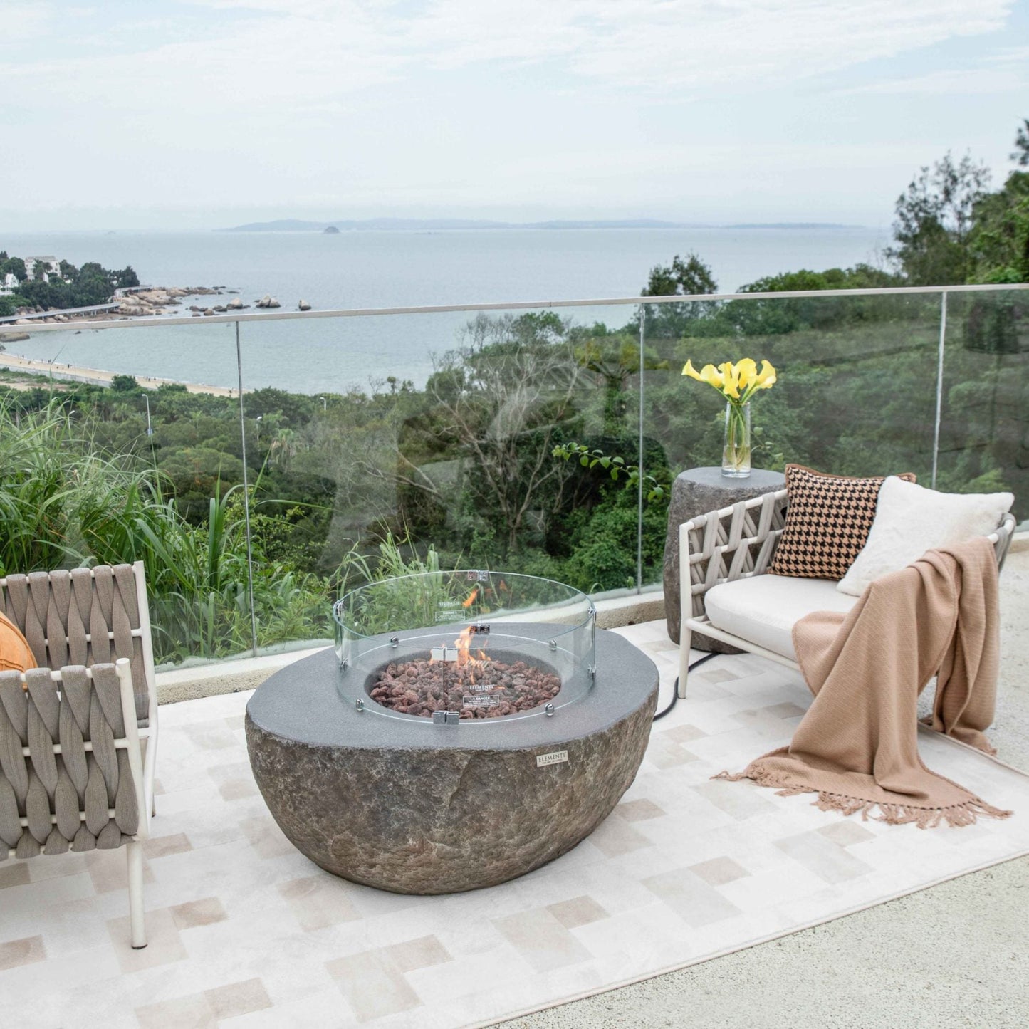 Outdoor patio with fire pit table and chairs overlooking a scenic view.