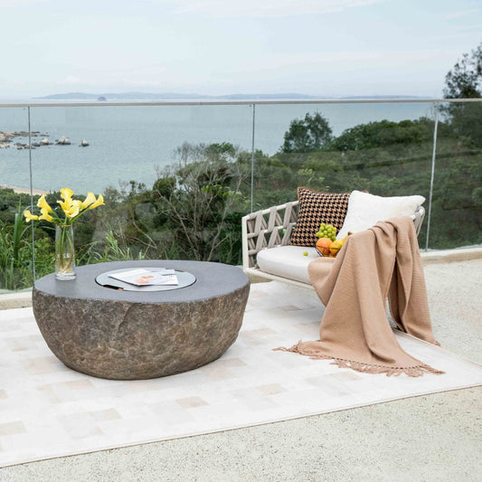 Outdoor patio with stone table, white chair, and scenic view of water and trees.