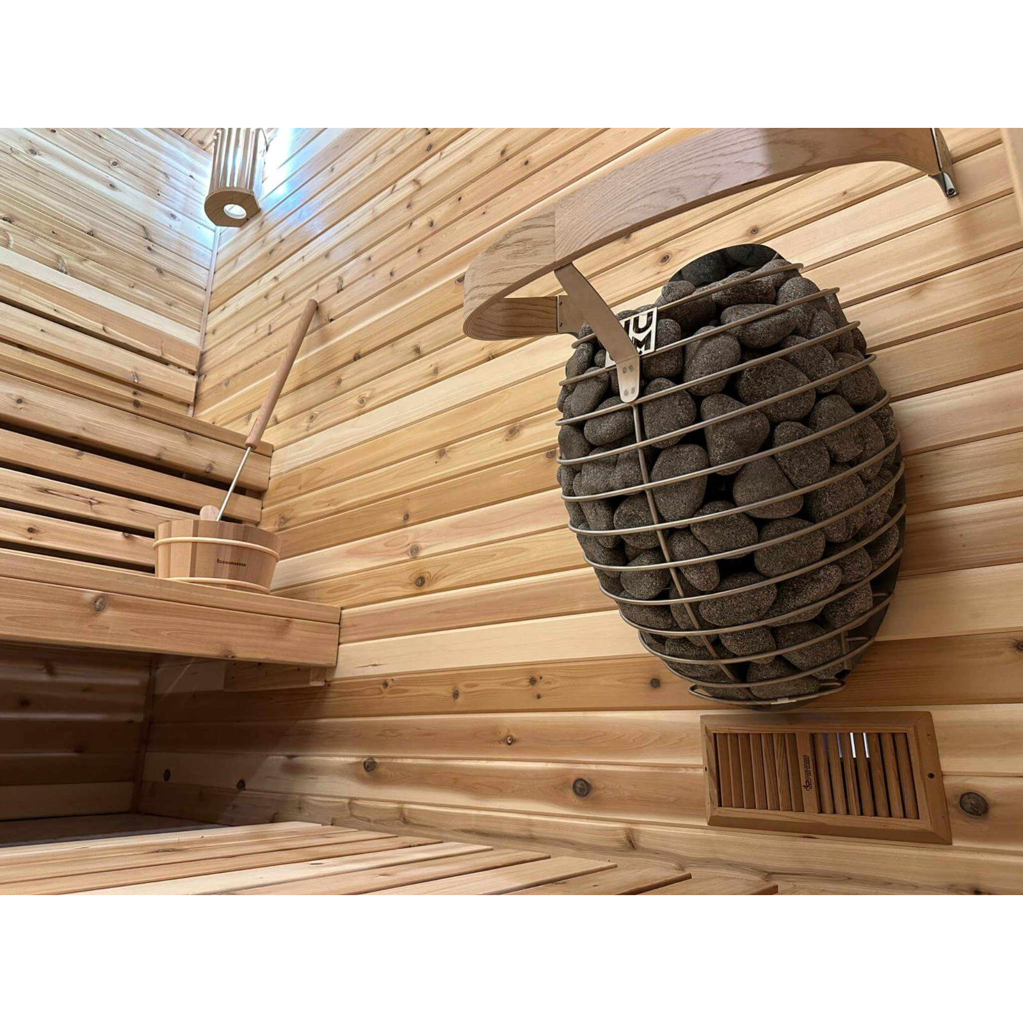 Side view of a wall-mounted electric sauna heater with a sleek, rounded design and stainless steel details, filled with sauna stones.