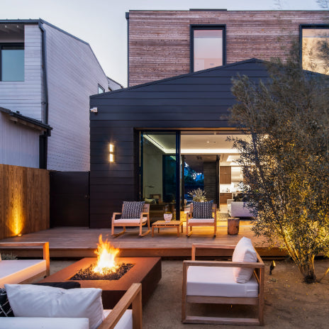Modern outdoor living space with fire pit, chairs, and a tree in front of a house.