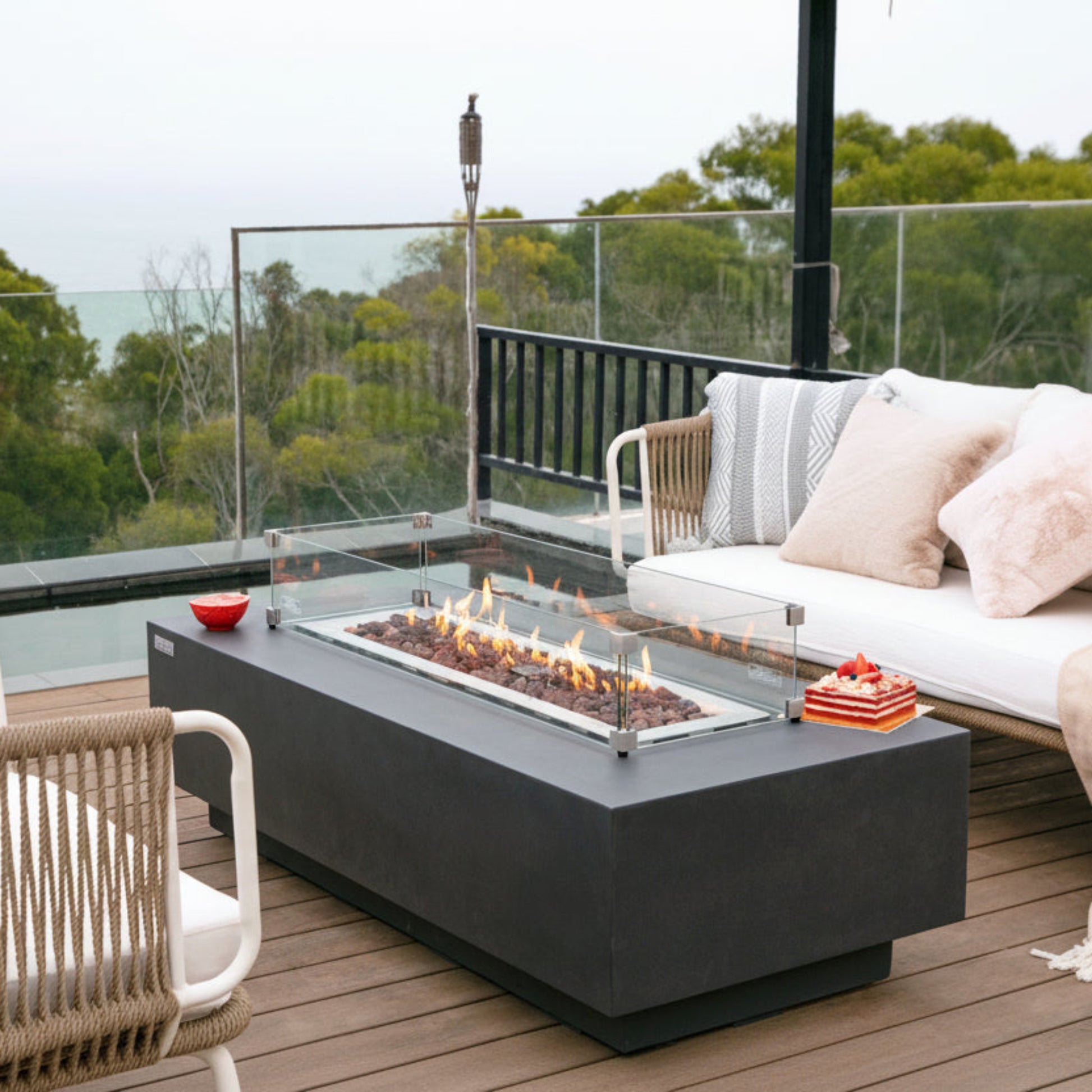 Outdoor patio setup with fire pit table, chairs, and sofa with cushions on a wooden deck.
