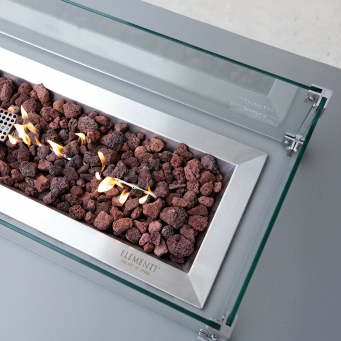 Modern gas fireplace with glass front and visible flames, featuring the Elementi brand.