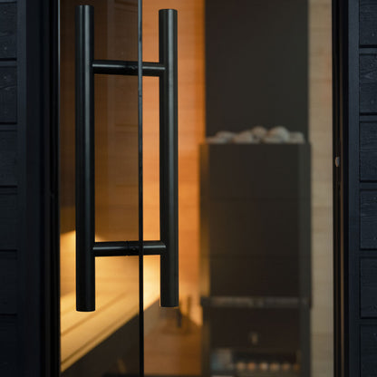 Close-up of a black sauna door handle on a glass door with a blurred interior background