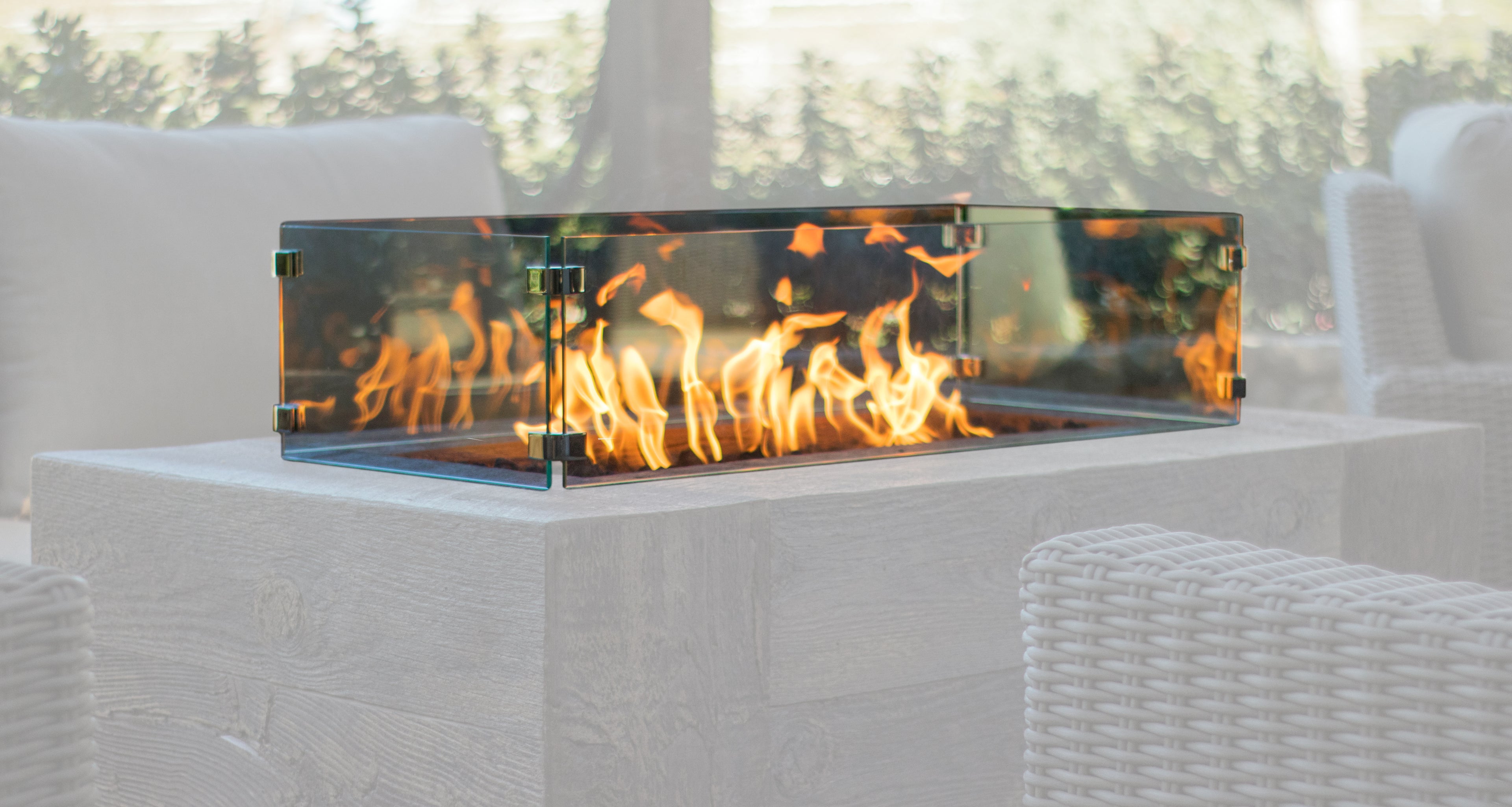 Outdoor fire pit with flames inside a transparent glass wind guard on a patio.